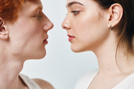 Young man and woman facing each other in closeup portrait with neutral expression on white background. Skin details and side profiles in intimate minimal composition for relationships.の写真素材