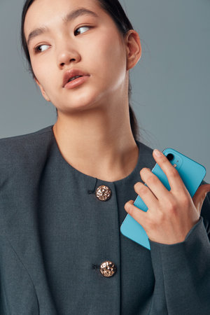 Young woman holding smartphone with blue case, looking sideways. Fashionable person wearing dark...