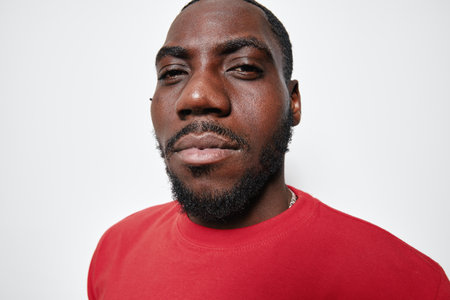 Portrait of confident black man with dark skin wearing red shirt looking at camera with slight smile...