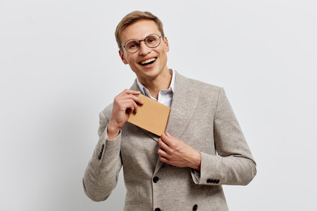 Confident smiling mature caucasian man with glasses in beige blazer holding small envelope against plain white background studio portrait. People lifestyle conceptの写真素材