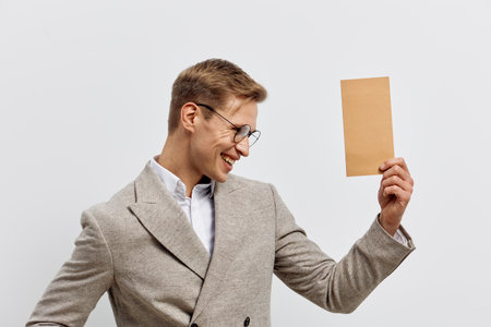 Smiling woman wearing glasses and a gray blazer holding a blank cardboard sign, posing against a plain white background in a studio setting.の写真素材