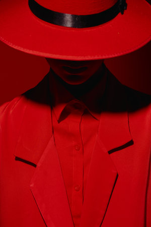 Figure in a red suit and wide-brimmed hat partially conceals the face showing minimal details. Dramatic lighting highlights textures of luxury fashion clothing. Creative concept for stylistic beauty.の写真素材