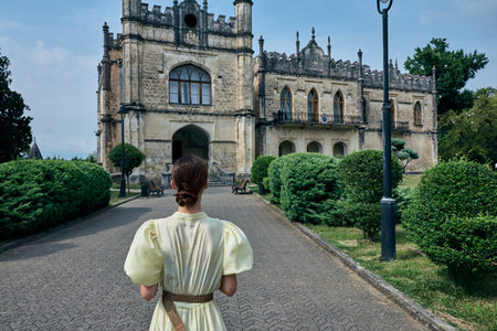 Woman vintage dress backview walking garden walkway historic mansion estate architecture...