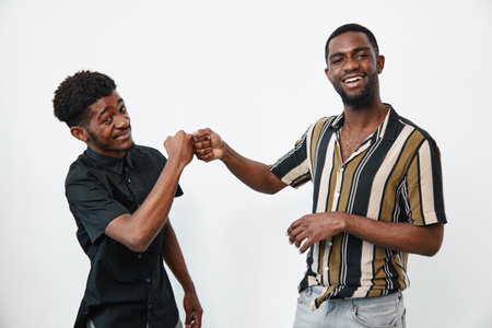 Two young black men with dark skin fist bumping and smiling in casual clothes on white background...