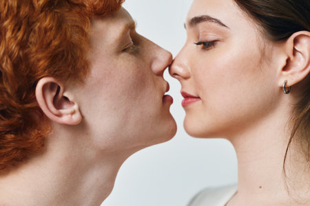 Young couple with red hair and brunette face close together with eyes closed for romantic moment and intimacy on light background. Man and woman with earrings and natural skin in love.の写真素材