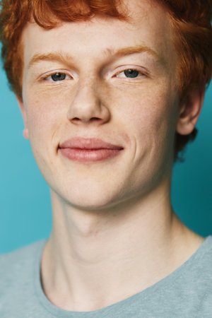 Portrait of young redhead man with freckles smiling with calm expression against blue background...