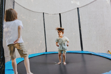 Happy children jumping on a trampoline, enjoying outdoor playtime with bright smiles and carefree energy in a sunny environment.の写真素材