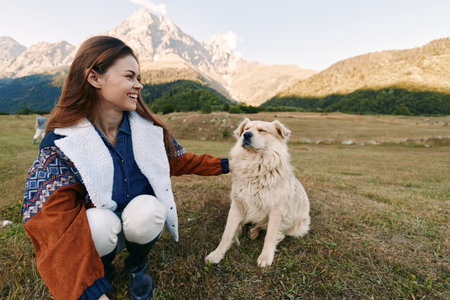 Woman dog mountain meadow outdoors pet companionship as she smiles while crouching beside fluffy dog during a hike in nature, relaxed portrait in grassy landscape and sunny daylight.の写真素材