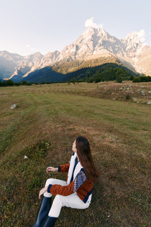 woman sitting on meadow facing mountain landscape in nature, autumn travel scene with long hair,...
