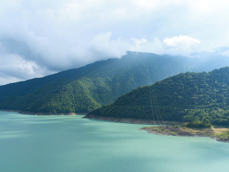 Lake and mountains with dense forest and turquoise water under dramatic clouds, aerial landscape view of reservoir shore and misty hills for nature, travel and outdoor scenery.の写真素材