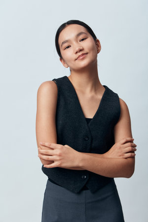 Young confident woman with crossed arms standing against plain background wearing dark vest and...
