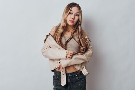 Young woman with long hair wearing casual beige jacket and knitted top posing with crossed arms on...