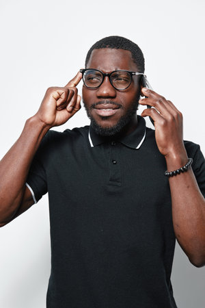 African American man with dark skin wearing glasses and black polo shirt thinking and talking on...