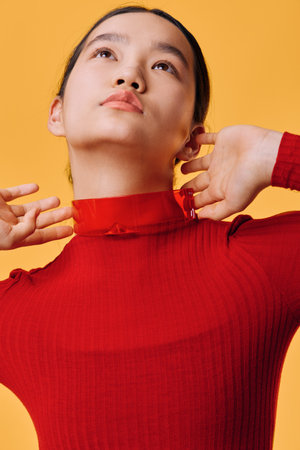 Woman in red sweater adjusting collar looking upwards with smooth skin and natural expression on yellow background, closeup portrait with modern minimalistic style and clean atmosphere.の写真素材