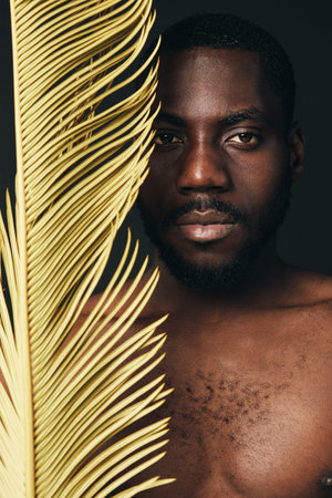 Creative conceptual portrait of African man with dark skin holding yellow palm leaf, visual style...