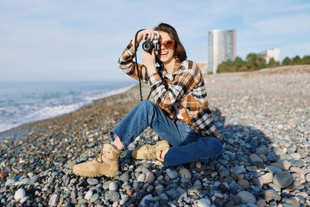 Female photographer on a pebble beach capturing a candid moment with a compact camera, wearing a...