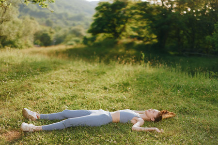 Young woman in activewear lying on grass in a serene nature setting, evoking tranquility and...