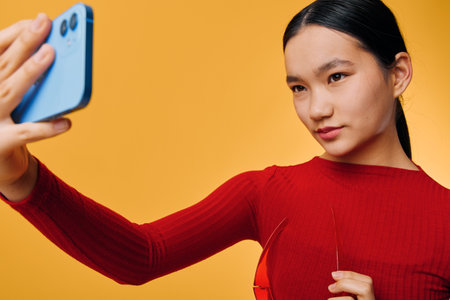 Young woman in red sweater taking selfie with smartphone, posing with focused expression against...