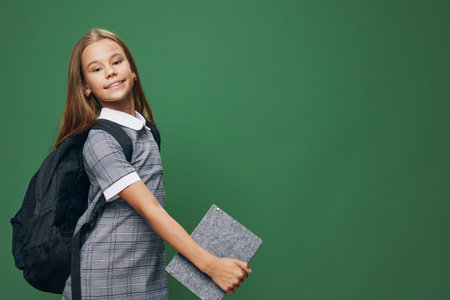 Girl student with backpack and book smiling with confidence standing against green background for...