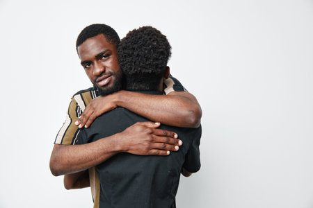 Two black men hugging each other in a warm embrace on white background. African ethnicity, dark...