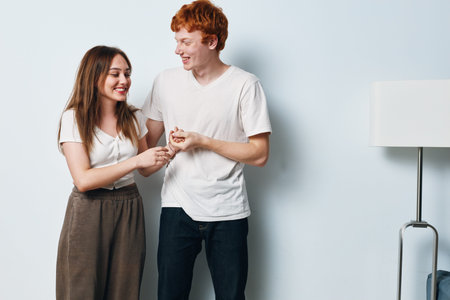 Young couple standing and smiling together in cozy home interior with modern white wall and floor lamp for lifestyle and happy relationship moments.の写真素材