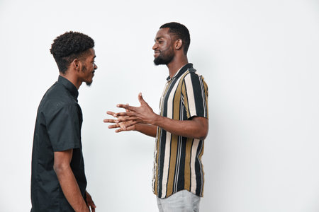 Two african american men with dark skin talking and gesturing in casual clothes against white...
