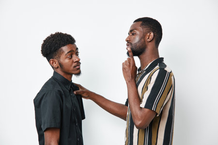 Two African American men with dark skin having a serious conversation in casual clothing against...