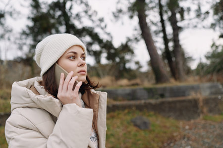 Woman, outdoor, phone, winter, coat, beanie, cold, landscape with trees as she talks on a mobile in...