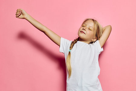 Young girl with long blonde hair stretching arms and closing eyes on pink background. She wears...