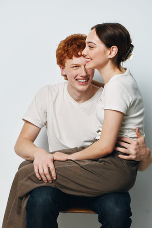 Young couple sitting together smiling and embracing with happiness casual clothing and relaxed pose against white background in studio setting.の写真素材