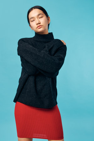 Young woman with eyes closed wearing black sweater and red skirt standing arms crossed on blue background for fashion portrait and casual style concept.の写真素材