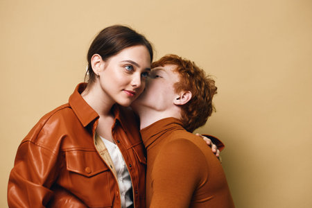 Couple, young man and woman in autumn clothing with affectionate gesture and intimacy on beige...
