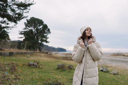 Woman in a long puffy winter coat outdoors along a coastline at dusk, enjoying the cool air and...