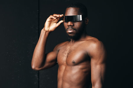 Creative conceptual portrait of shirtless African man wearing futuristic visor glasses in visual style with dark background and confident pose for modern fashion.の写真素材