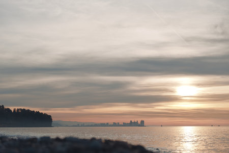 Sunset over a calm sea with a distant coast and soft clouds, warm glow on the water creates a tranquil landscape for nature and reflective momentsの写真素材
