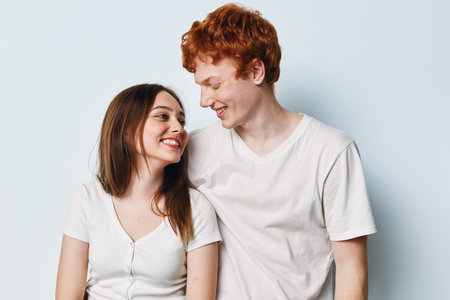 Young couple, smiling and looking at each other, wearing casual white t shirts against plain light background. Friendship, happiness and connection between man and woman.の写真素材