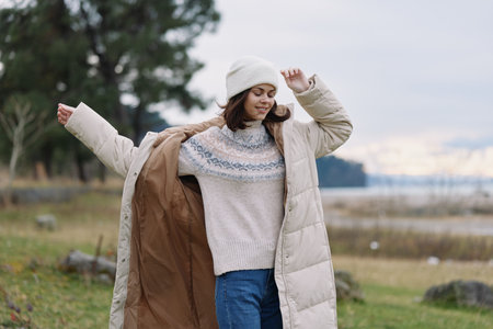 Woman wearing a long beige puffer coat and knit sweater outdoors, enjoying a windy day by the shore, casual winter fashion and cozy cold weather style for a relaxed lifestyle shootの写真素材