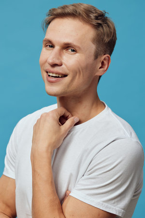 Confident young man with short light brown hair wearing white casual t-shirt looking at camera smiling isolated on vibrant blue background studio portrait. People lifestyle conceptの写真素材