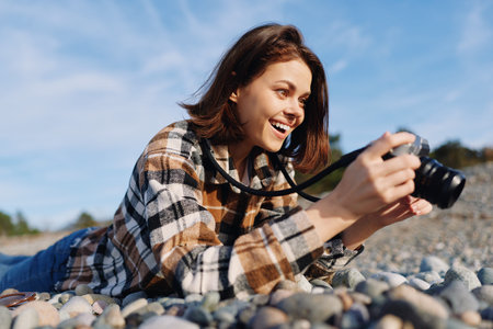 Camera, photography, outdoors, woman, lying, pebbles, beach, hobby, lens, smiling, candid moment under sunny sky with camera in hand, capturing a joyful outdoor scene during a relaxed photoshoot onの写真素材