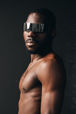 African man with dark skin and muscular body wearing futuristic silver visor in creative conceptual visual style. Portrait with strong lighting and modern artistic expression.の写真素材