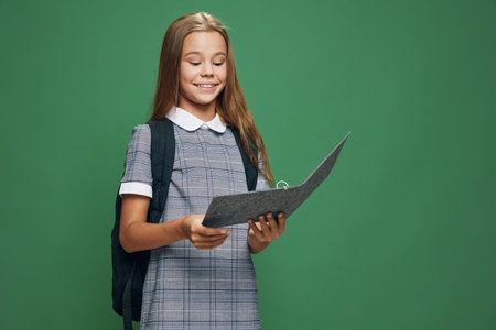Schoolgirl student with backpack reading book or notebook with smile on green background for education, learning, knowledge and study at school or academy.の写真素材