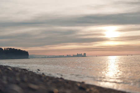 Sunset, water, horizon paint a tranquil coastal scene with silhouettes along the coastline, calm waves along the shoreline and reflective light on the ocean at duskの写真素材