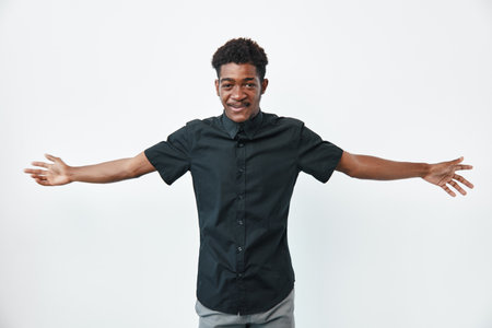 African man with dark skin wearing black shirt standing with arms wide open smiling on white background. Young adult male, casual clothing and positive expression.の写真素材