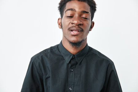 Young black man with dark skin wearing black shirt posing with eyes closed and relaxed expression on white background in studio portrait.の写真素材