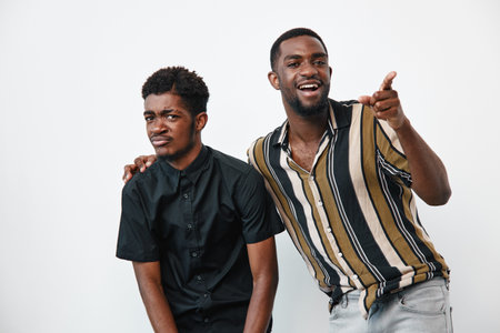 Two african men with dark skin posing together in casual clothes on white background. One man wears black shirt, other striped shirt, smiling and pointing with hand.の写真素材