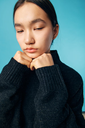 Young woman in black sweater with closed eyes expresses sadness and contemplation on blue background. Portrait, emotion, and fashion with natural light and calm mood.の写真素材