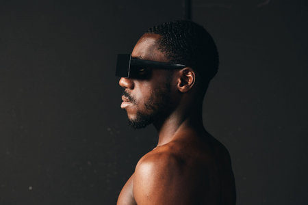 Creative visual designer style portrait of black African man with dark skin wearing futuristic black sunglasses in profile on dark background with dramatic lighting.の写真素材