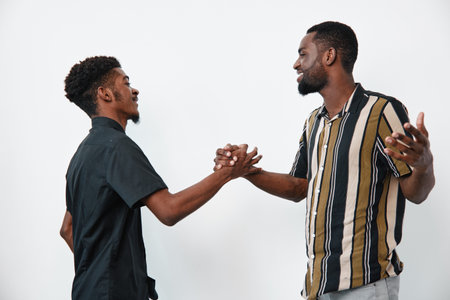 Two black men with dark skin shaking hands and smiling in casual clothes on white background for friendship, greeting and positive connection between friends.の写真素材