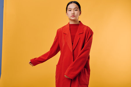 Portrait of young woman in red oversized blazer standing against yellow background with serious expression and natural makeup, fashion style with minimalistic studio setup.の写真素材