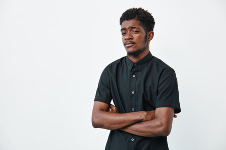 Young black man with dark skin and curly hair wearing black shirt standing with crossed arms on...
